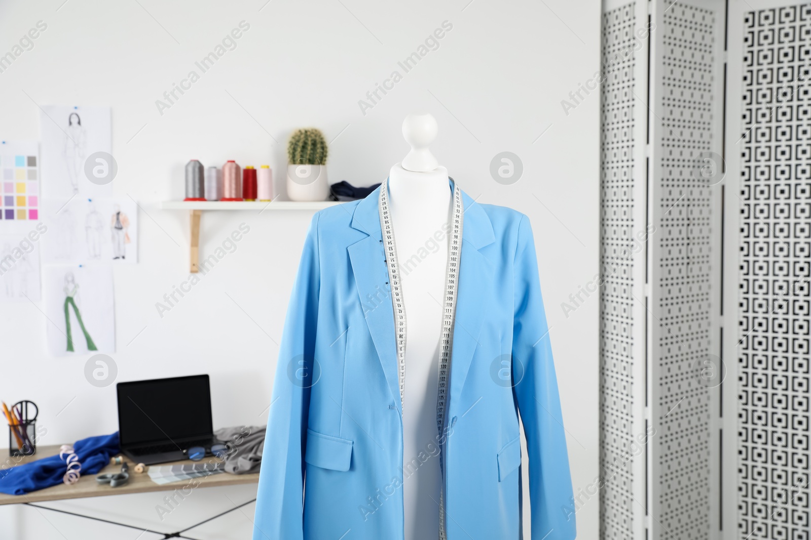 Photo of New blue jacket and measuring tape on mannequin in fashion designer`s workshop