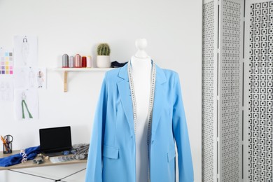 Photo of New blue jacket and measuring tape on mannequin in fashion designer`s workshop