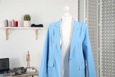 Photo of New blue jacket and measuring tape on mannequin in fashion designer`s workshop