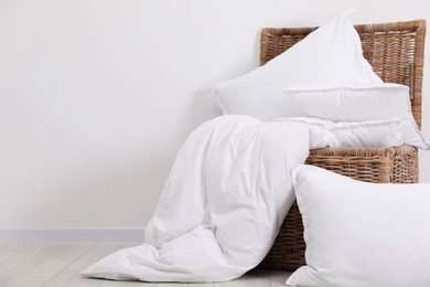 Photo of Clean pillows, duvet and storage basket on floor near white wall. Space for text