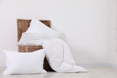 Photo of Clean pillows, duvet and storage basket on floor near white wall. Space for text