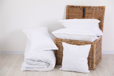 Photo of Clean pillows, duvet and storage basket on floor near white wall