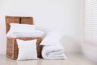 Clean pillows, duvet and storage basket on floor near white wall