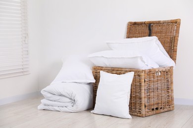 Photo of Clean pillows, duvet and storage basket on floor near white wall