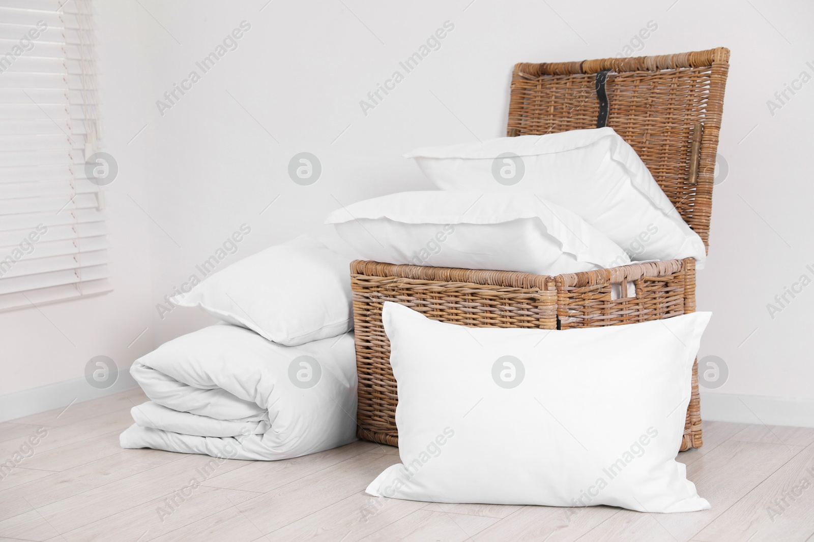 Photo of Clean pillows, duvet and storage basket on floor near white wall