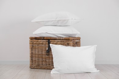 Photo of Clean pillows and storage basket on floor near white wall