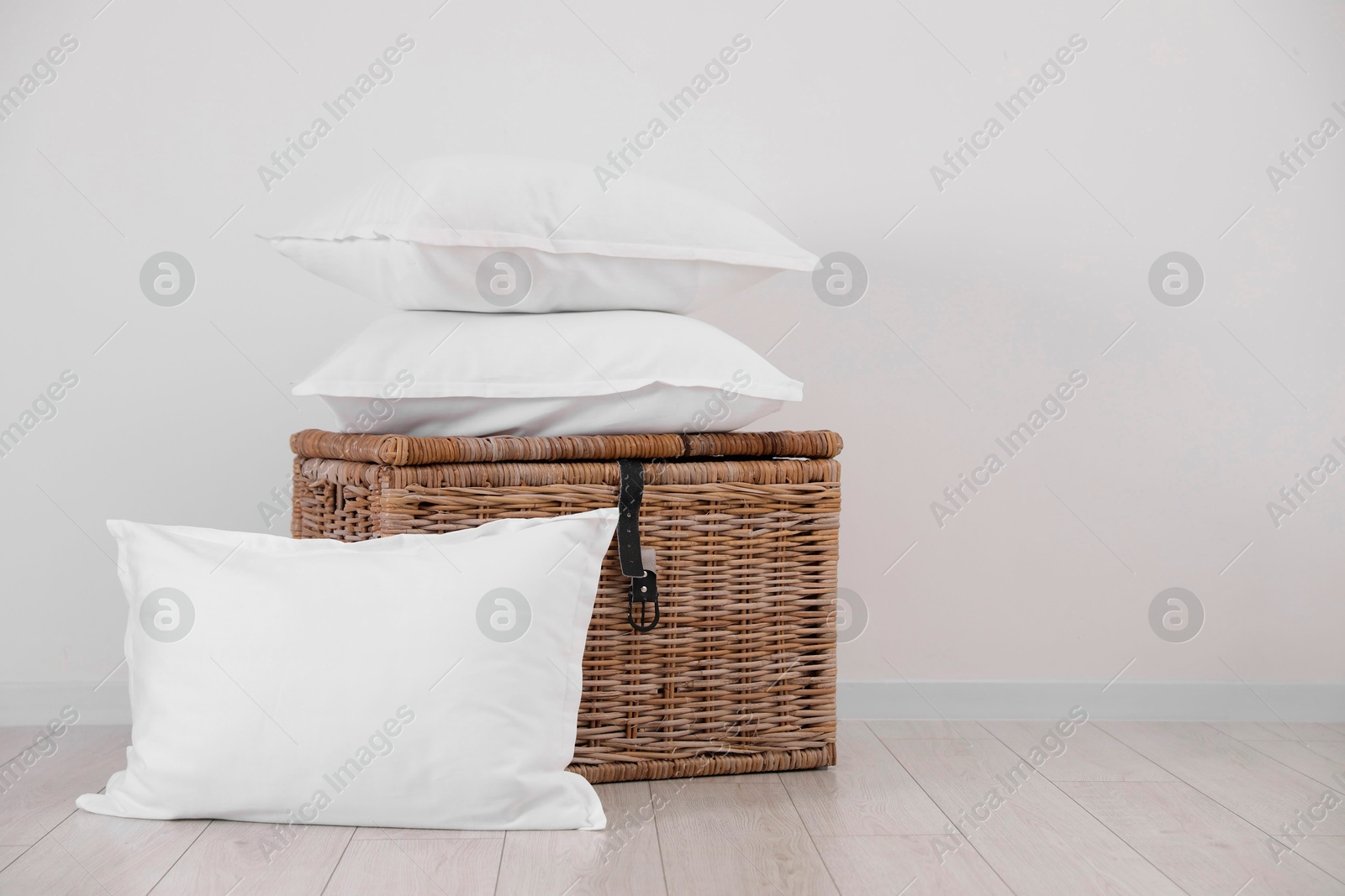 Photo of Clean pillows and storage basket on floor near white wall