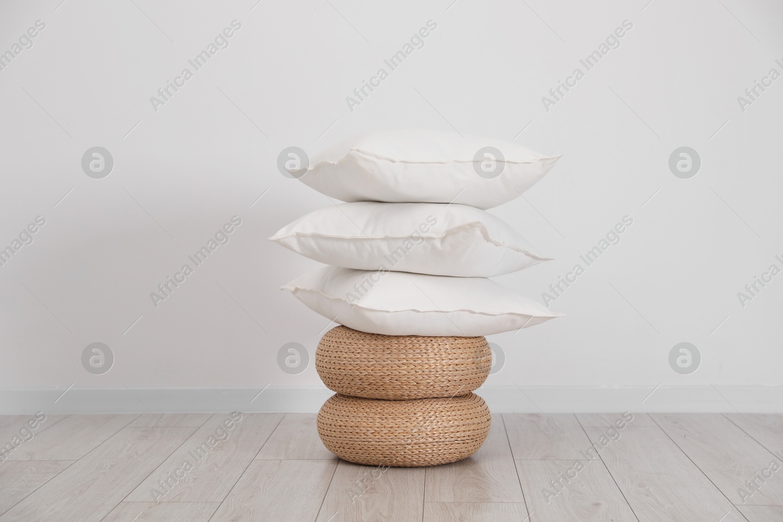 Photo of Stack of clean pillows on wicker poufs near white wall