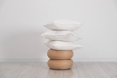 Stack of clean pillows on wicker poufs near white wall