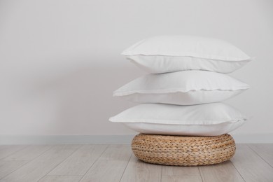 Photo of Stack of clean pillows on wicker pouf near white wall. Space for text