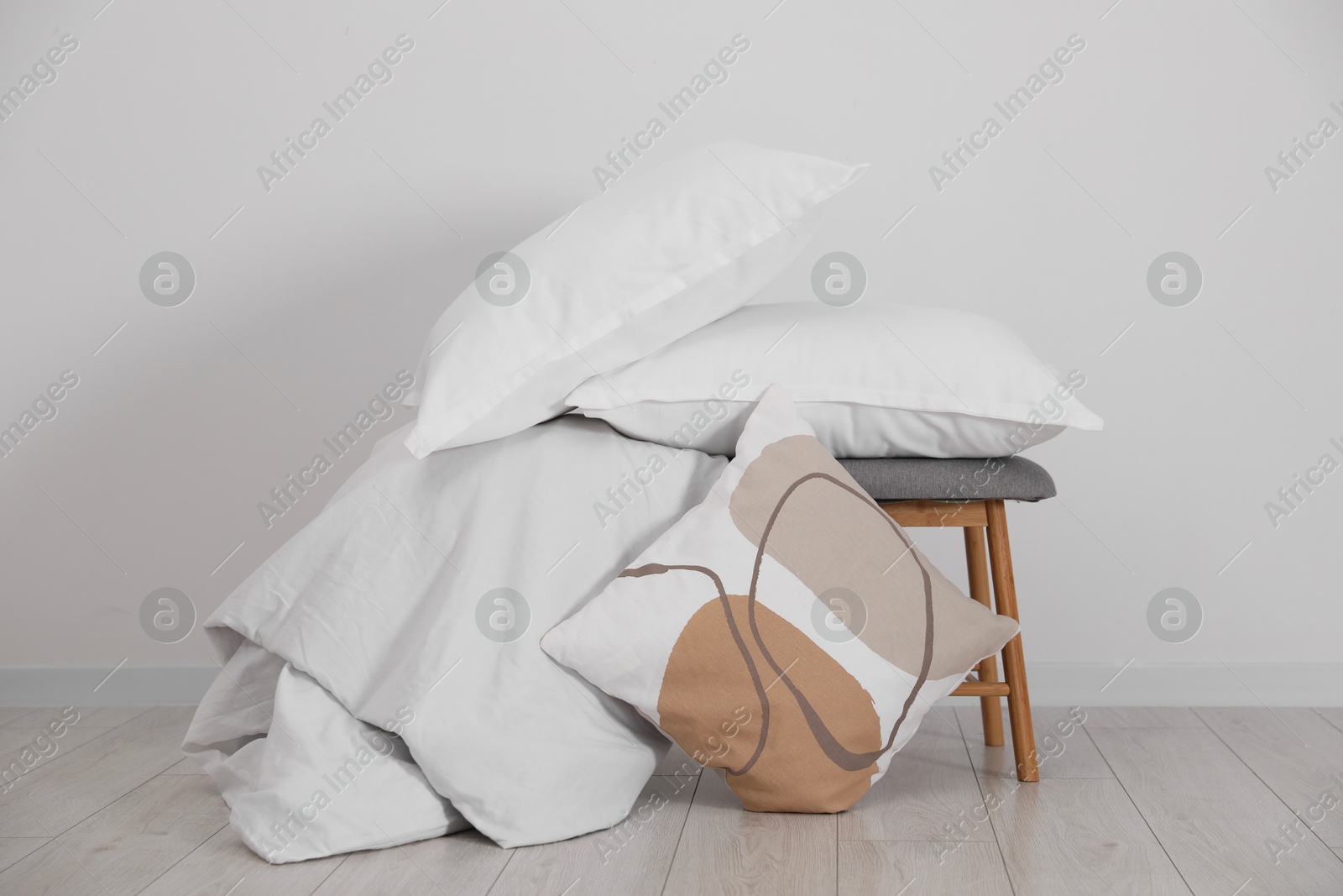 Photo of Clean pillows, blanket and stool on floor near white wall