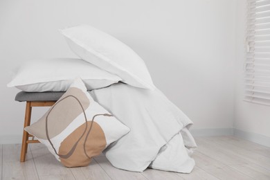 Photo of Clean pillows, blanket and stool on floor near white wall. Space for text