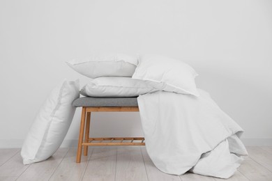 Clean pillows, blanket and storage bench on floor near white wall