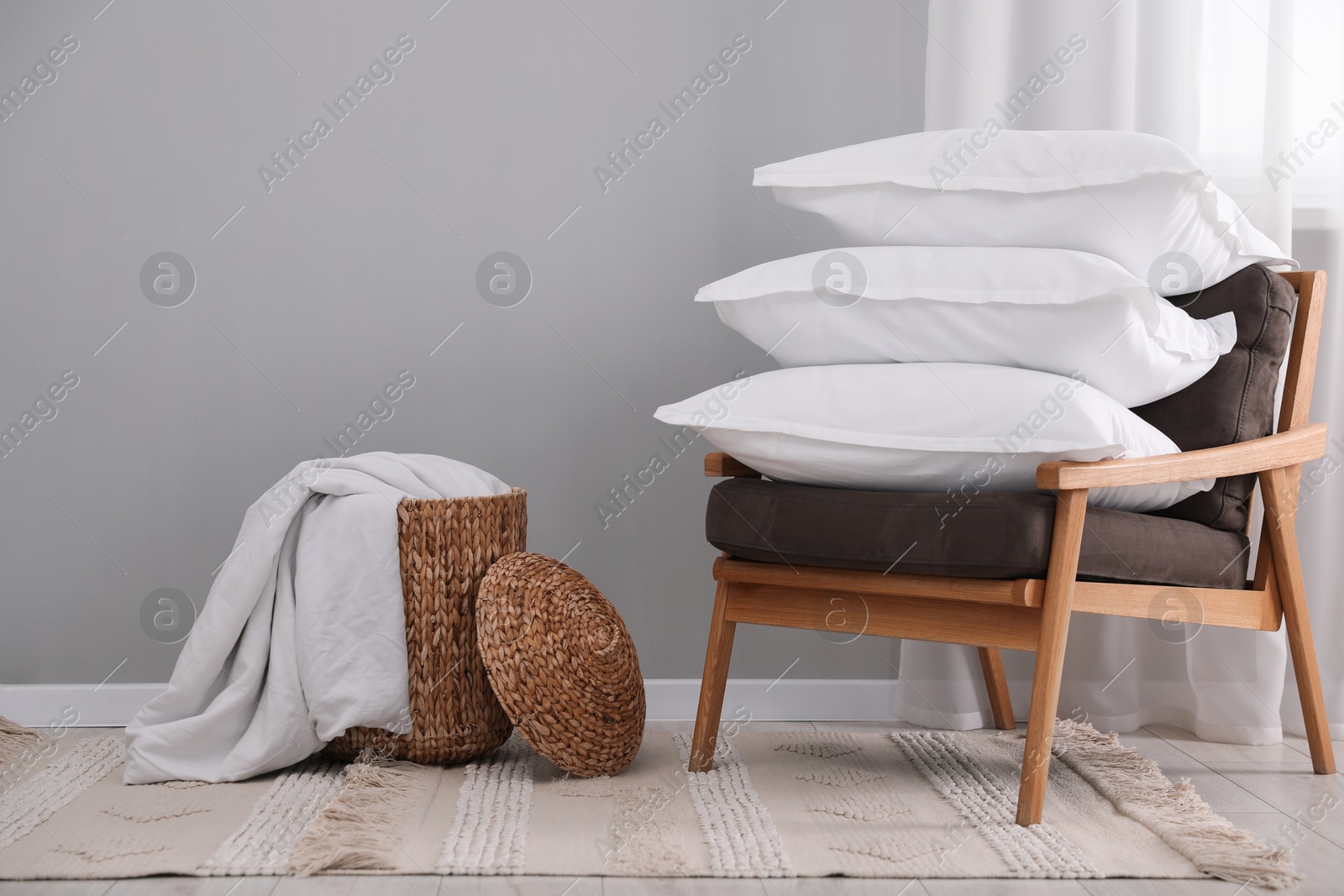 Photo of Stack of white pillows, armchair and wicker basket on floor indoors