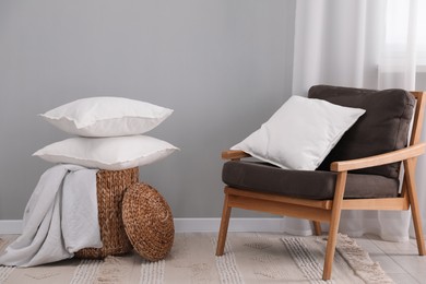 Stack of white pillows, armchair and wicker basket on floor indoors