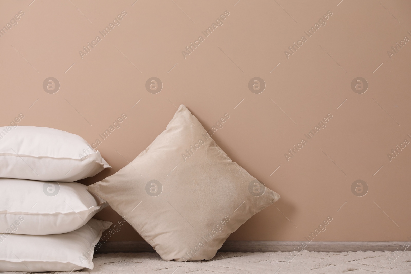 Photo of Soft pillows on floor near beige wall. Space for text