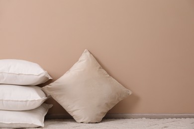 Soft pillows on floor near beige wall. Space for text