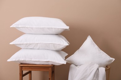 Stack of pillows, stool, storage basket and blanket near beige wall