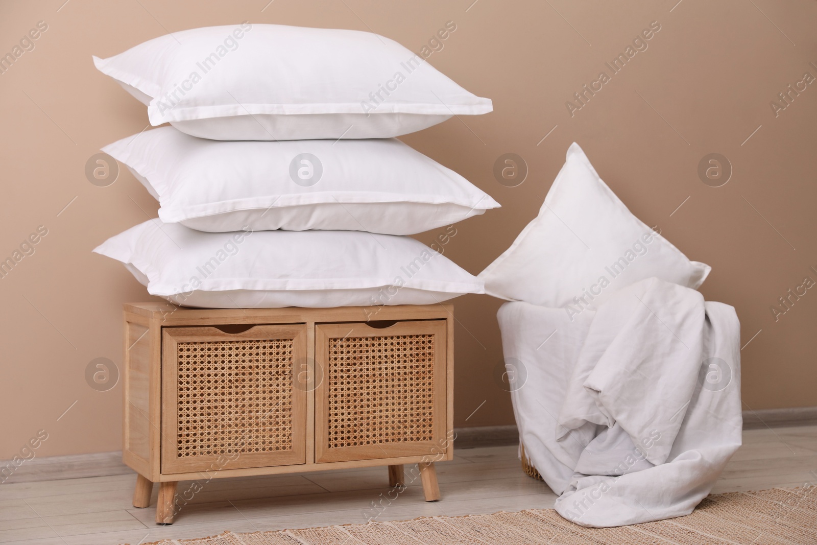 Photo of Stack of pillows, storage cabinet, basket and blanket near beige wall