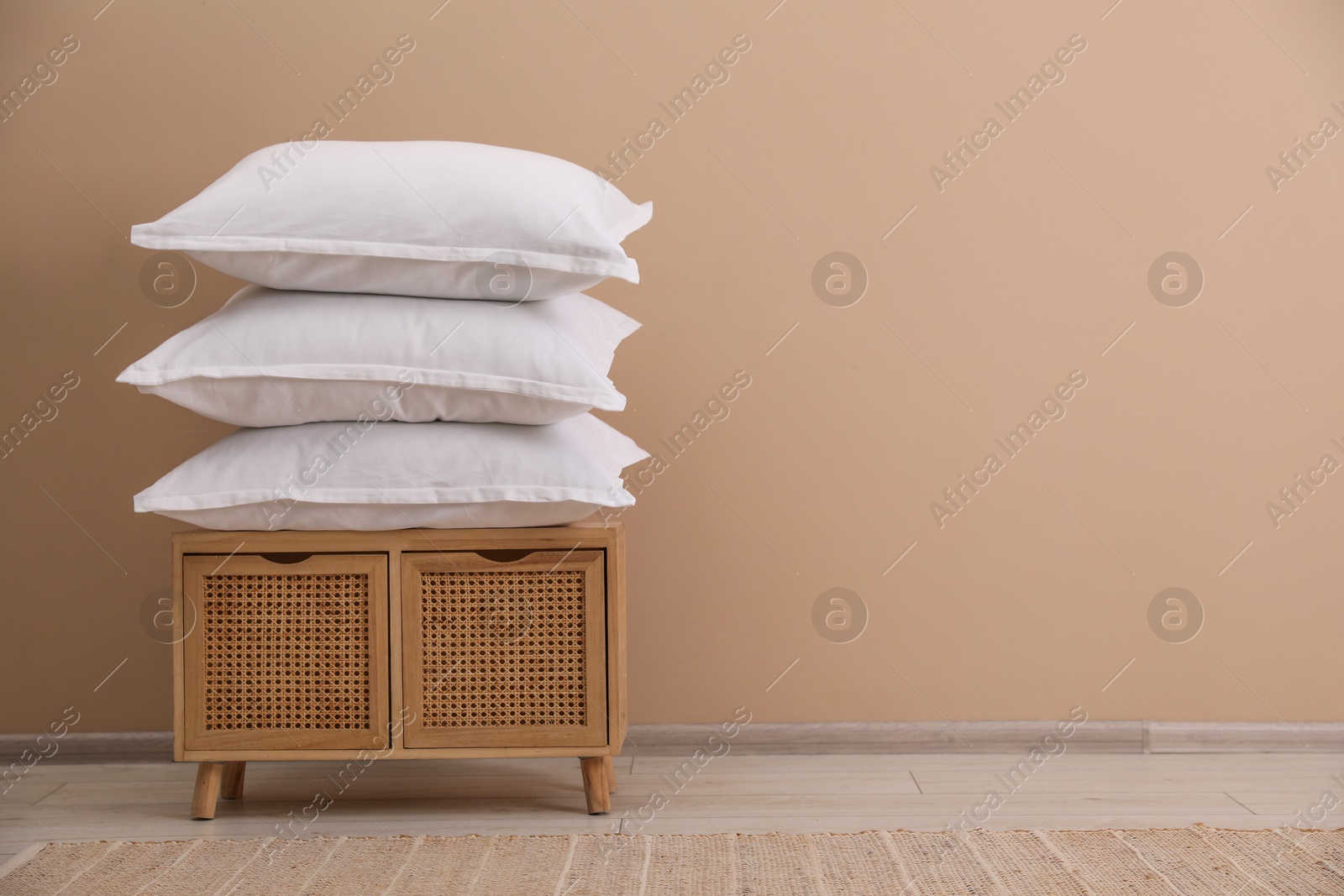 Photo of Stack of pillows on storage cabinet near beige wall. Space for text