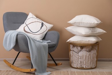 Photo of Pillows, armchair, storage basket and blanket near beige wall