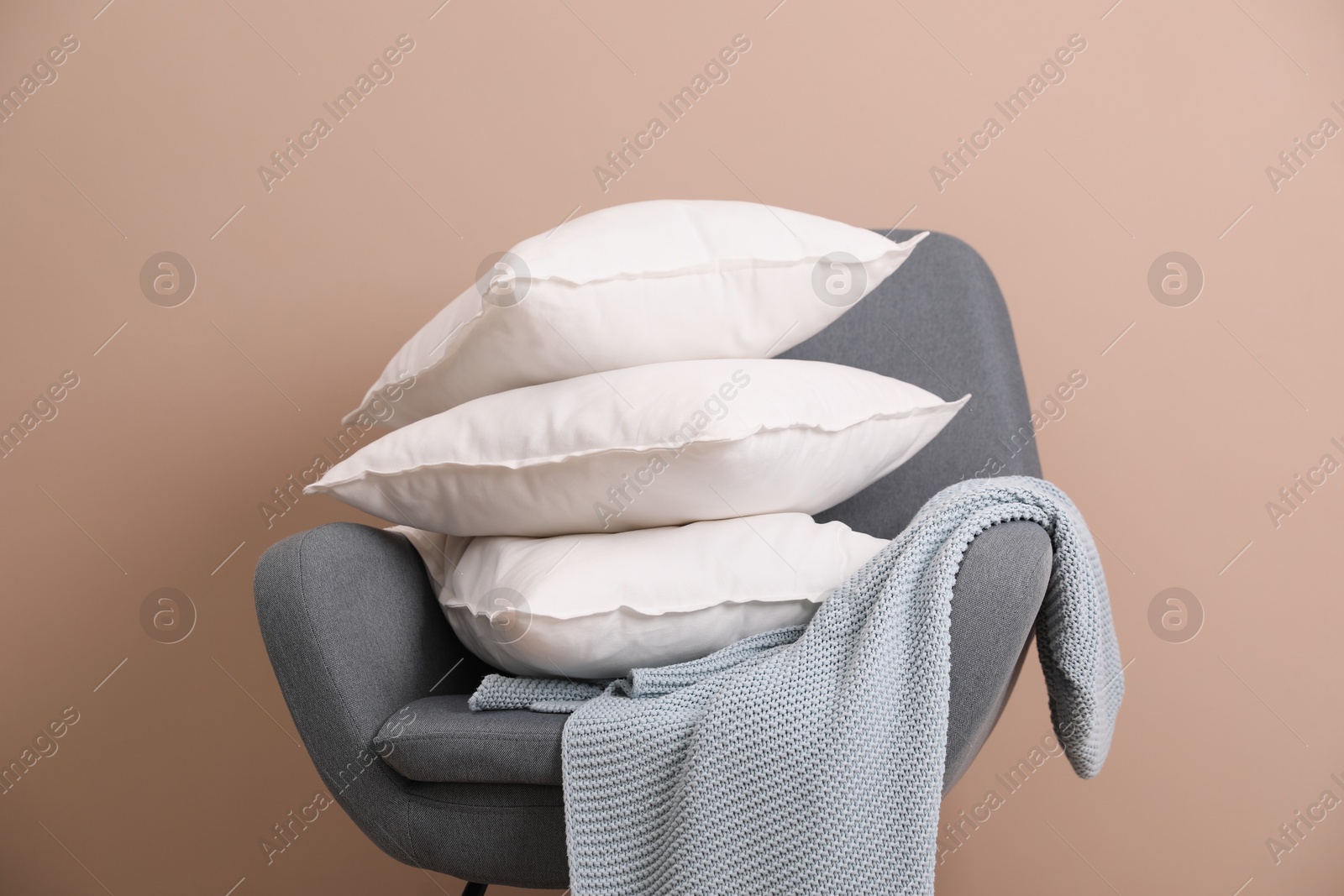 Photo of Stack of pillows, armchair and blanket near beige wall