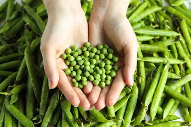 Photo of Woman holding fresh green peas near pods, top view