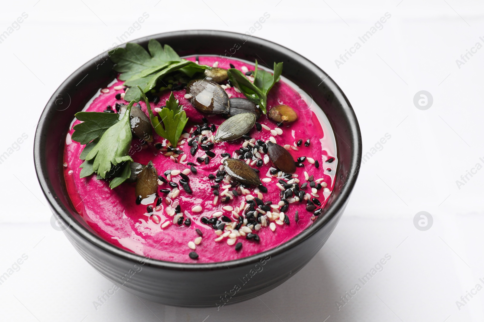 Photo of Tasty beetroot hummus, parsley and sesame in bowl on white table, closeup