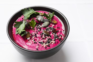 Tasty beetroot hummus, parsley and sesame in bowl on white table, closeup