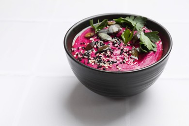 Photo of Tasty beetroot hummus, parsley and sesame in bowl on white table, closeup. Space for text