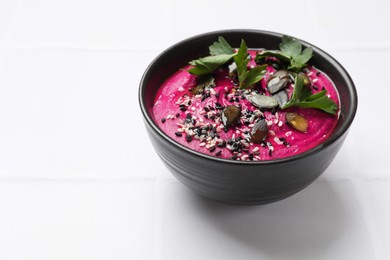 Photo of Tasty beetroot hummus, parsley and sesame in bowl on white table, closeup. Space for text