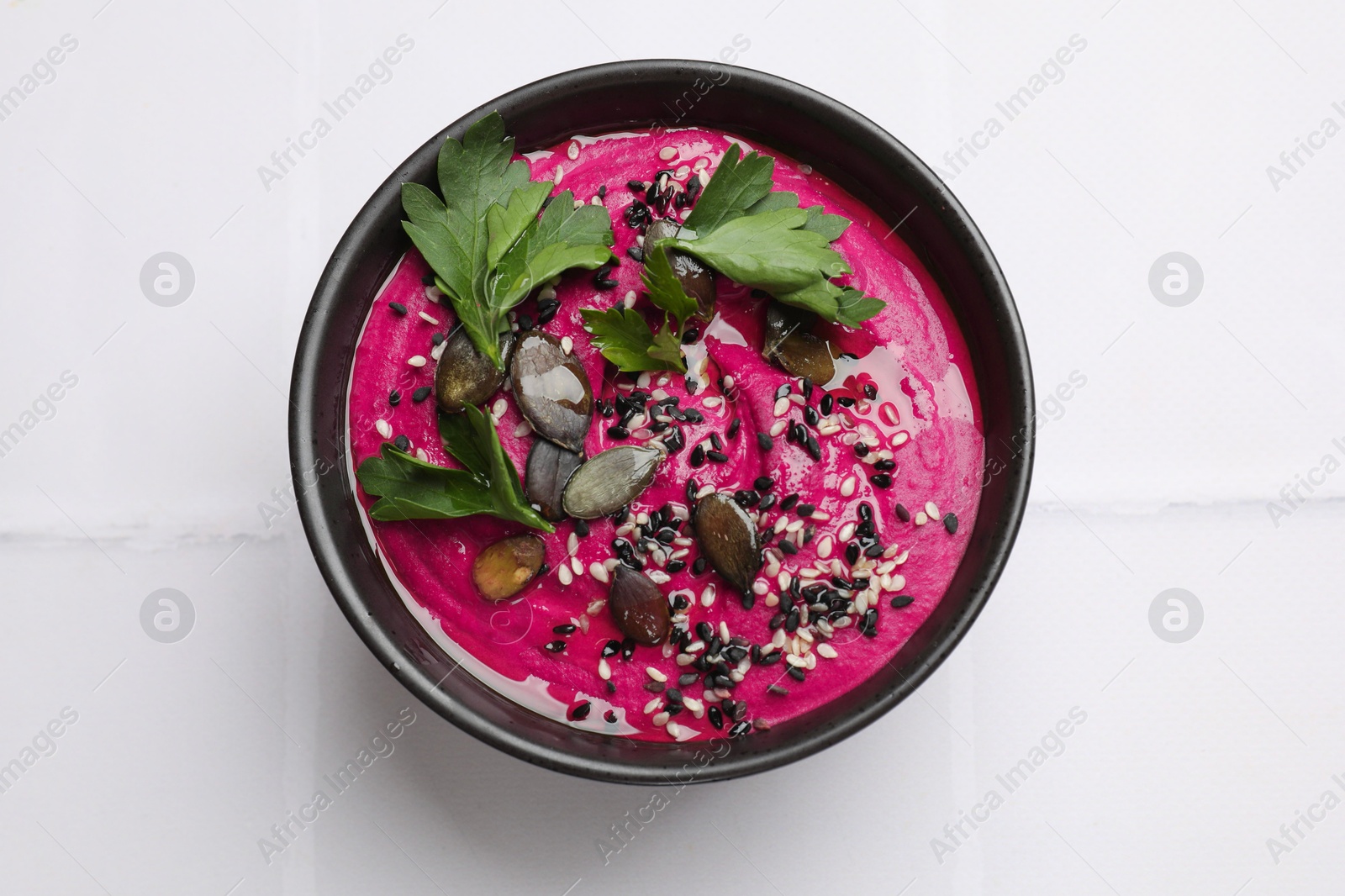 Photo of Tasty beetroot hummus, parsley and sesame in bowl on white table, top view