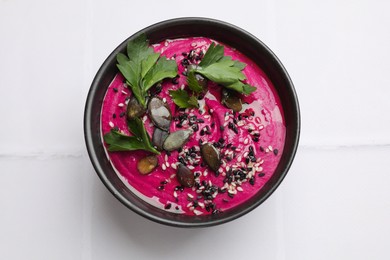 Tasty beetroot hummus, parsley and sesame in bowl on white table, top view