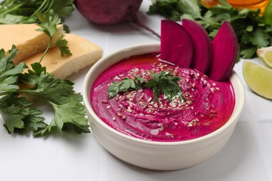 Tasty beetroot hummus in bowl and products on white table, closeup