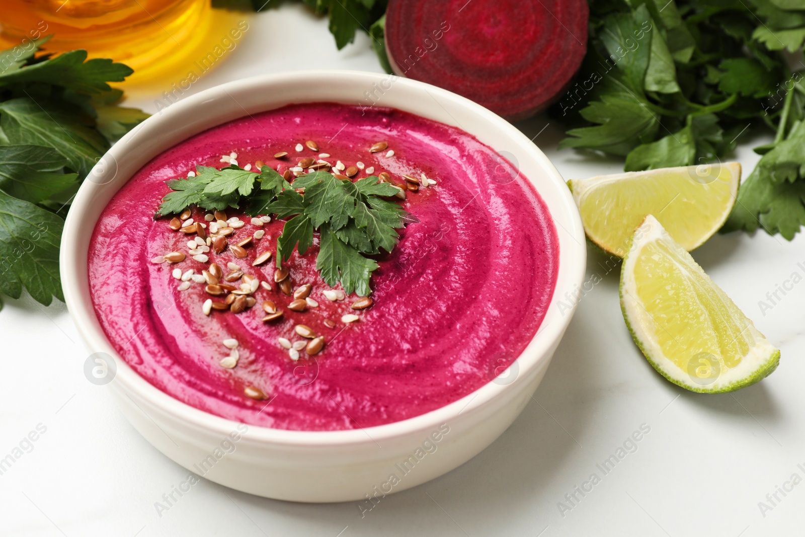 Photo of Tasty beetroot hummus in bowl and products on white marble table, closeup