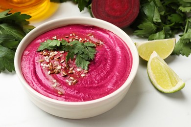 Photo of Tasty beetroot hummus in bowl and products on white marble table, closeup