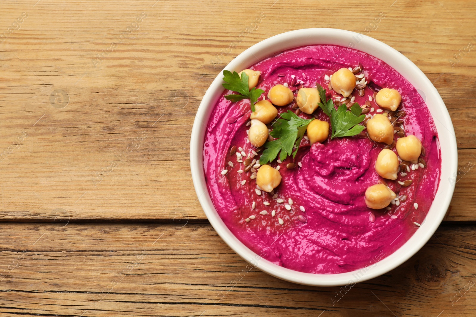 Photo of Tasty beet hummus with chickpeas and parsley in bowl on wooden table, top view. Space for text