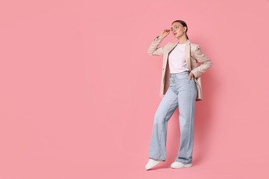 Stylish woman in beige jacket and jeans on pink background, space for text