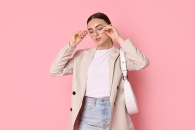 Stylish woman in beige jacket with bag on pink background