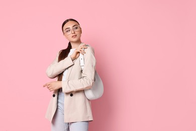 Stylish woman in beige jacket with bag on pink background, space for text