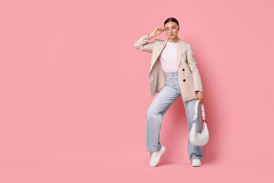 Stylish woman in beige jacket with bag on pink background, space for text