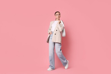 Photo of Stylish woman in beige jacket with bag on pink background