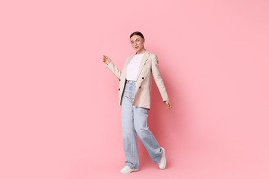 Stylish woman in beige jacket and jeans on pink background