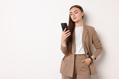 Woman in beige suit using smartphone on white background, space for text