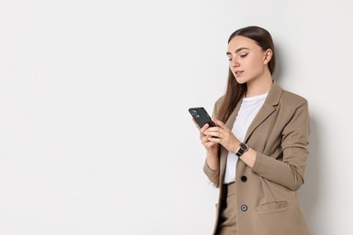 Photo of Woman in beige suit using smartphone on white background, space for text