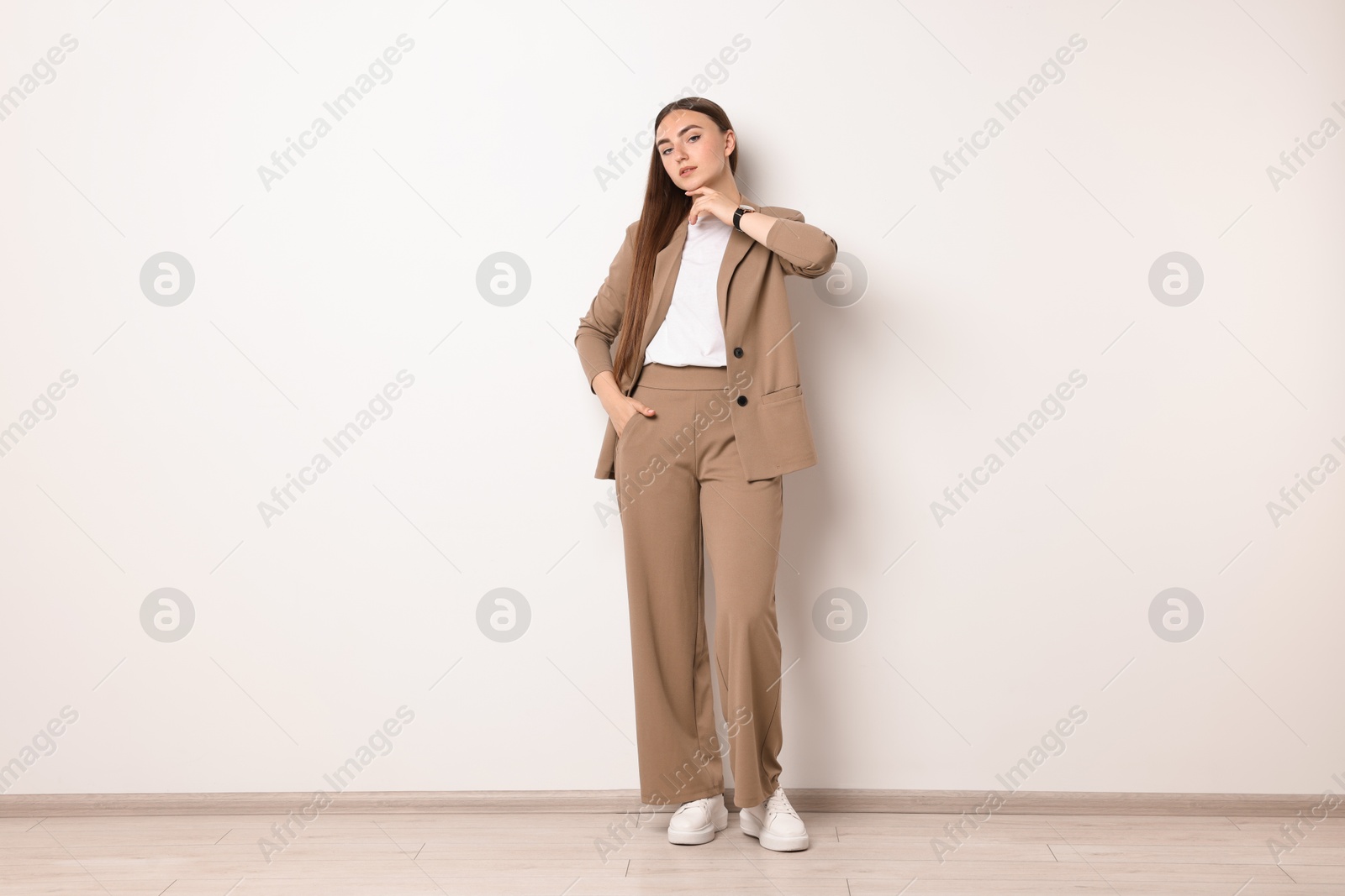 Photo of Beautiful woman in beige suit near white wall indoors