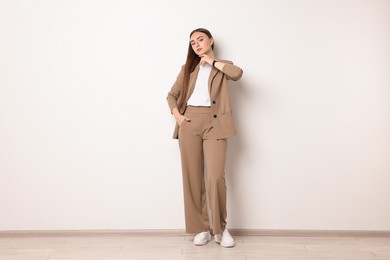 Beautiful woman in beige suit near white wall indoors