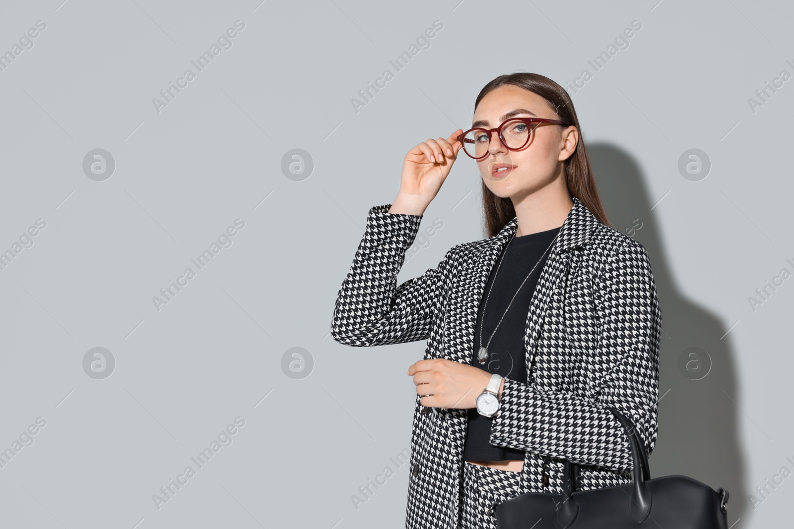 Photo of Beautiful woman in stylish suit and glasses with bag on gray background, space for text