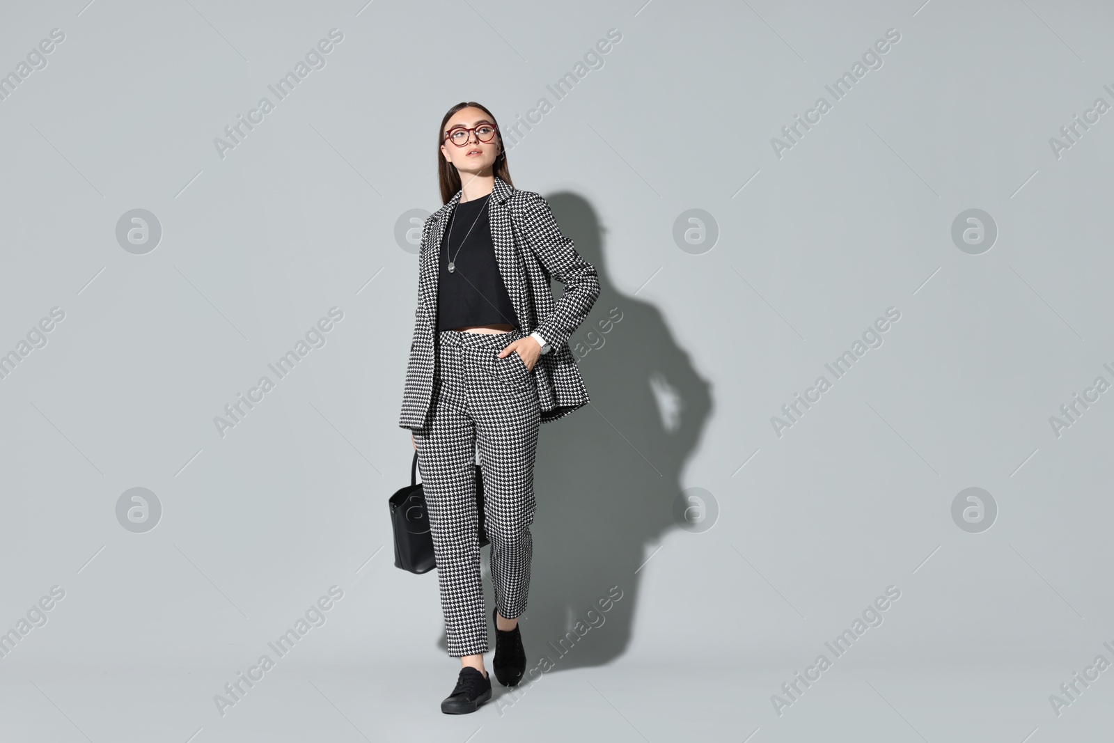 Photo of Beautiful woman in stylish suit and glasses with bag on gray background