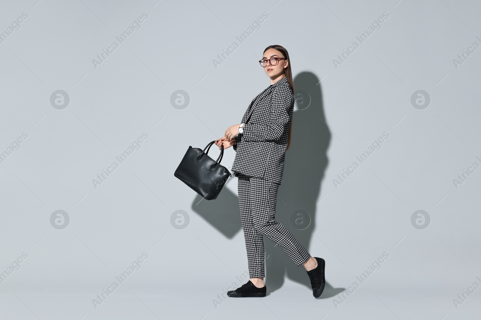 Photo of Beautiful woman in stylish suit and glasses with bag on gray background